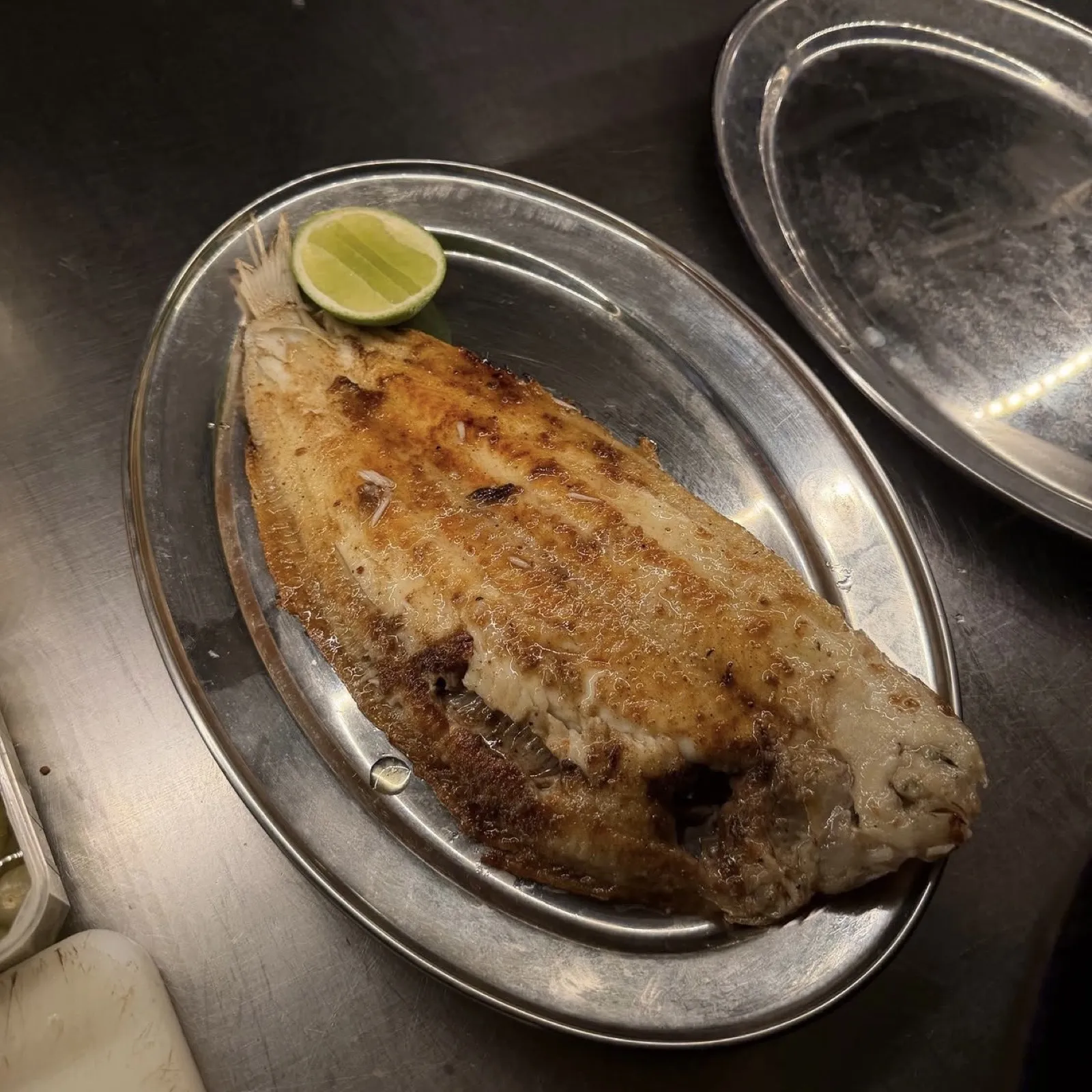 Poisson entier grillé servi sur plat en inox avec citron vert