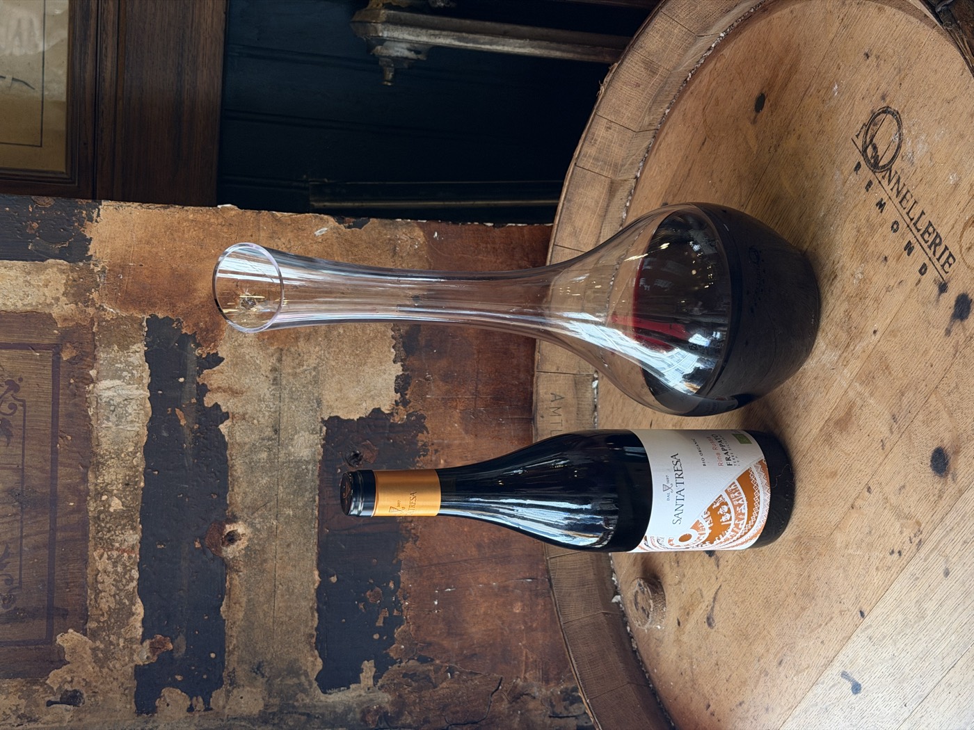 Bouteille de vin nature et carafe posées sur un tonneau devant un mur patiné